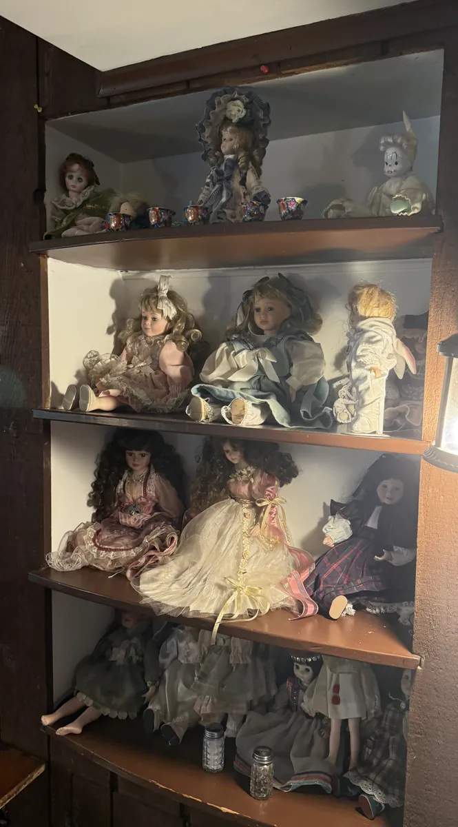 A built-in corner cabinet filled with porcelain dolls in lace dresses