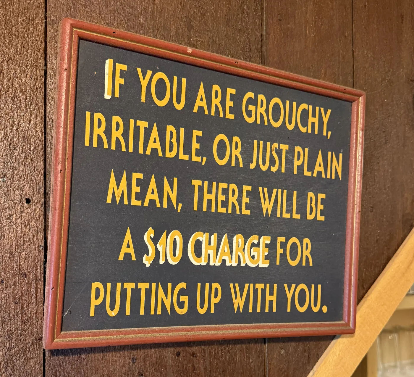 A painted sign reading: if you are grouchy, irritable, or just plain mean, there will be a ten dollar charge for putting up with you
