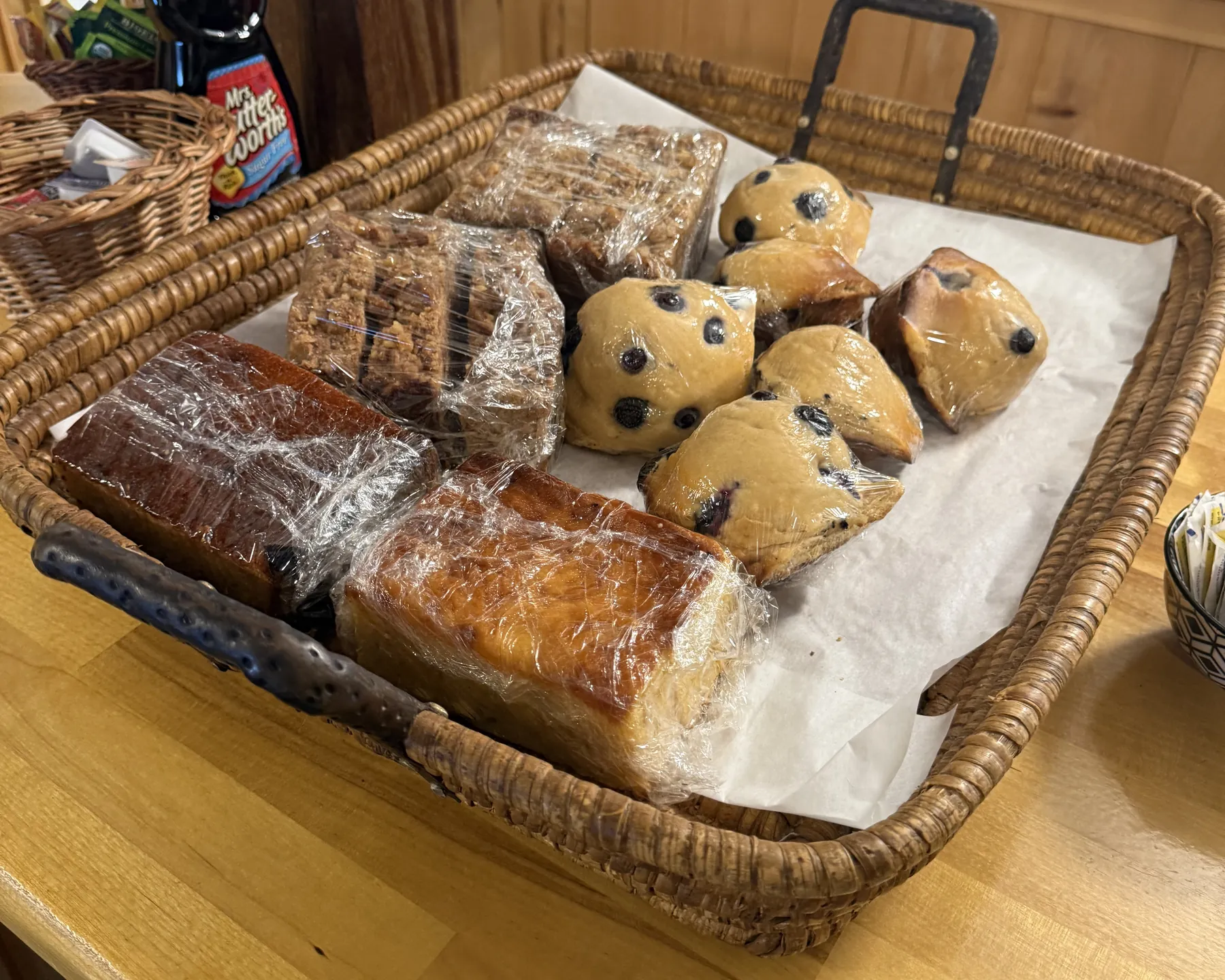 A wicker tray of blueberry muffins, coffee cake and wrapped quick breads