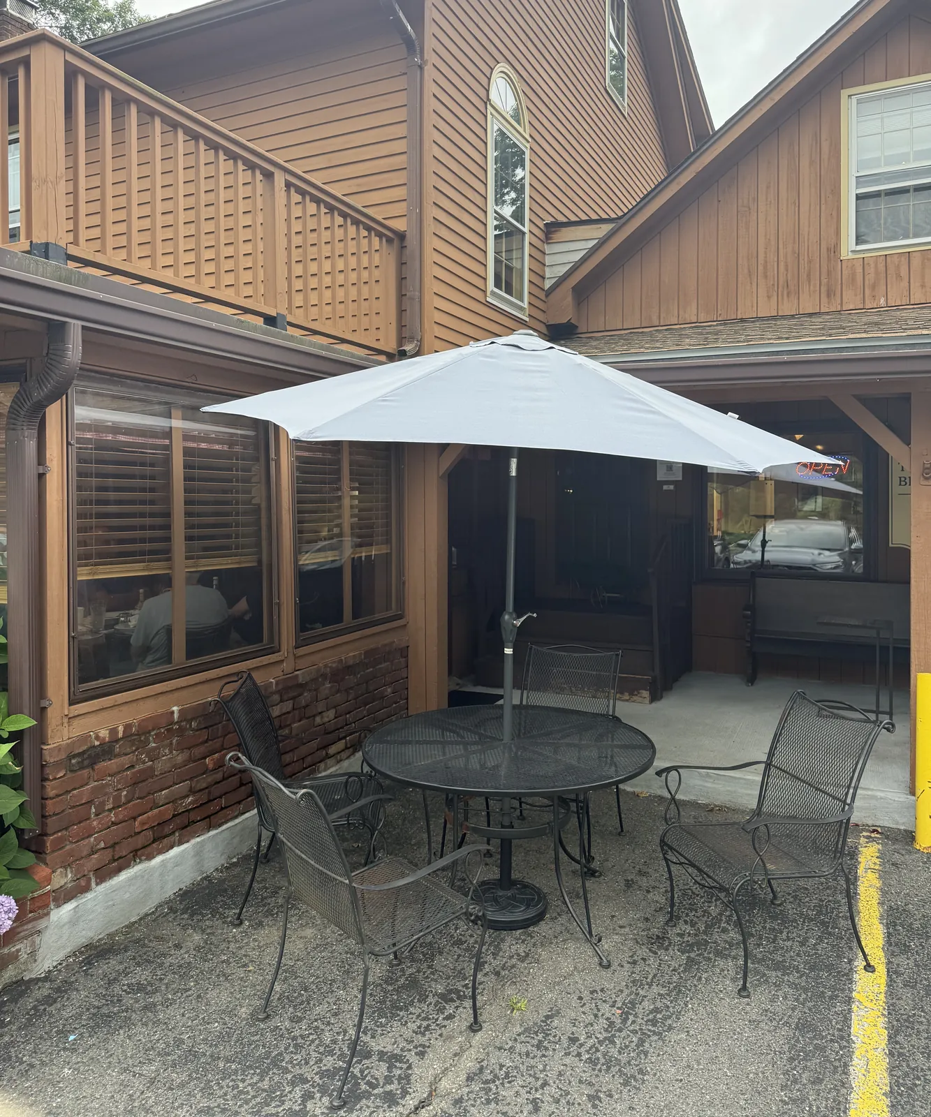 A metal table and chairs under a pale umbrella beside the building